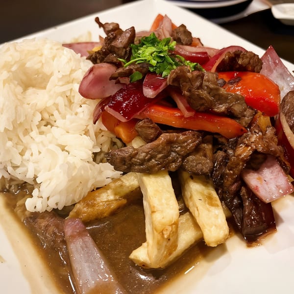 Peruvian Lomo Saltado with beef, red onions, tomatoes, fries, and rice on a white plate.