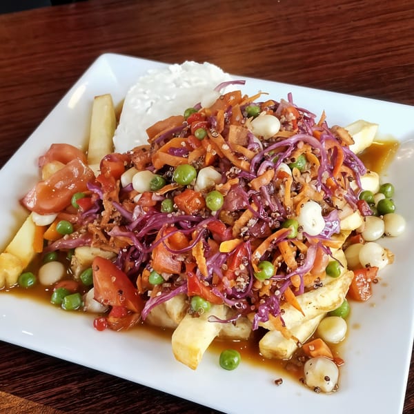 Peruvian poutine with french fries, vegetables, and white sauce on a white rectangular plate.