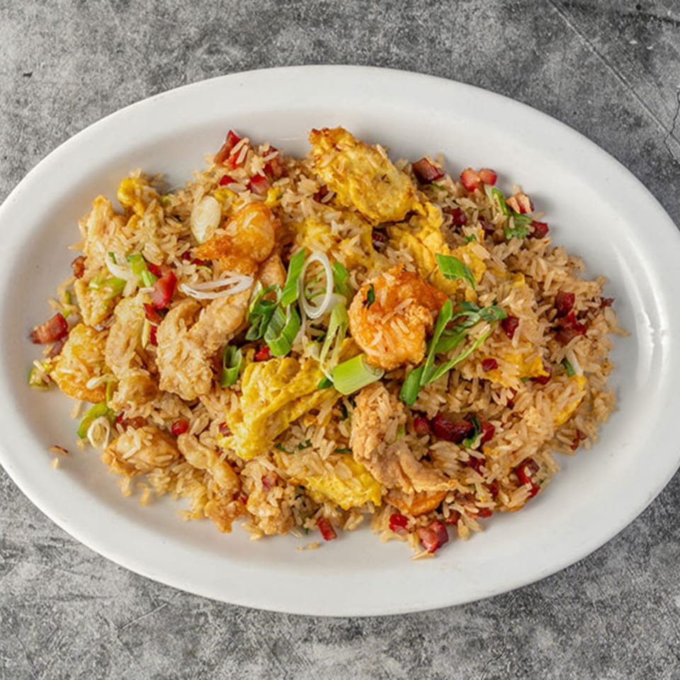 Peruvian fried rice (Arroz Chaufa) with chicken, shrimp, egg, and green onions on a white plate.