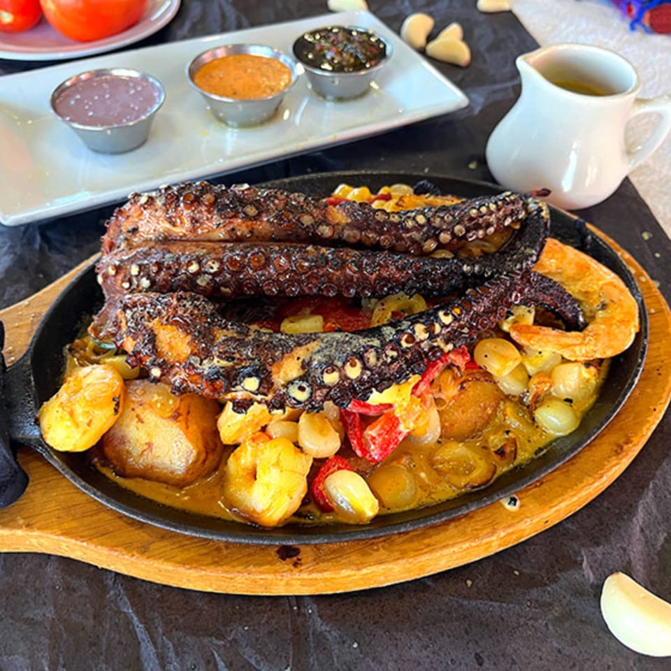 Peruvian grilled octopus and shrimp with potatoes and peppers in a sizzling skillet.