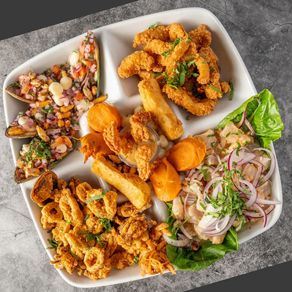 A white platter with various Peruvian dishes, including ceviche, fried seafood, and mussels.