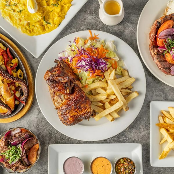 A Peruvian feast with roasted chicken, fries, salad, seafood, steak, and various sauces.