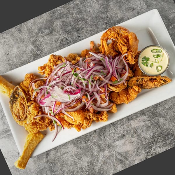 Chios Peruvian Grill's fried seafood platter with red onions, cilantro, and a side of creamy sauce.