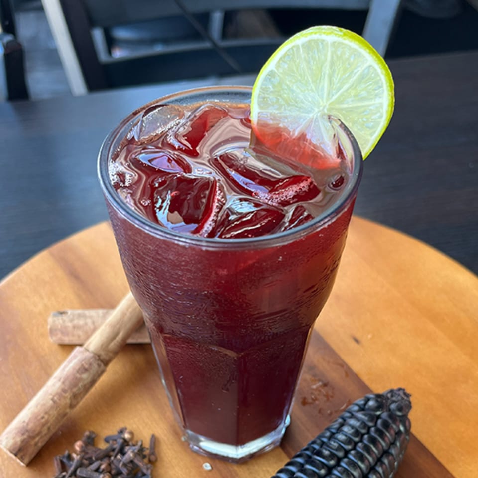 A glass of Chicha Morada, a Peruvian purple corn drink, garnished with a lime slice.