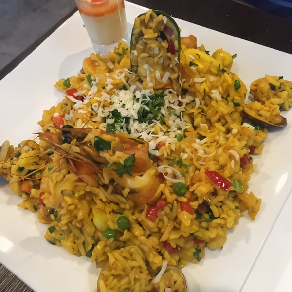 Peruvian seafood paella with shrimp, mussels, peas, and red peppers, topped with cheese and parsley.