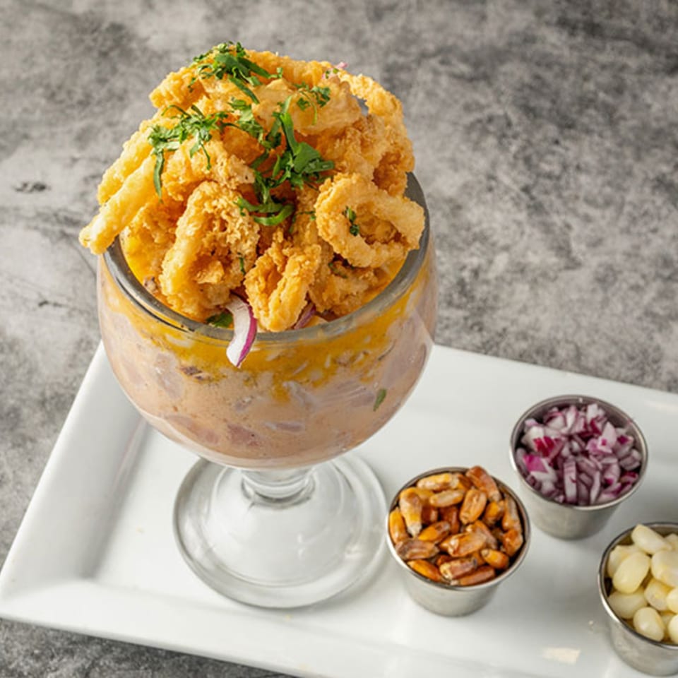 Peruvian ceviche with fried calamari, red onions, and corn in a glass on a white tray.